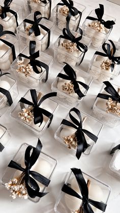 many small white cakes with black ribbons on display in glass containers, all decorated with pearls and bows