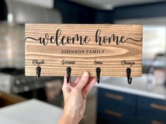 a person holding up a wooden sign that says, welcome home with hooks on it