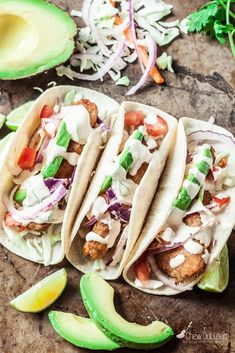 three fish tacos with avocado and cilantro on a cutting board