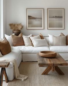 a living room with white couches and pillows on the walls, two pictures above them