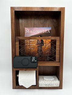 a wooden shelf with a cell phone and magazine on it, next to a toilet paper dispenser