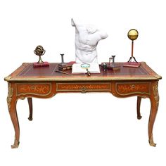 an antique desk with various items on it and a statue in the backgrouf