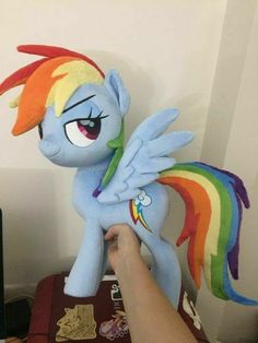 someone is holding a rainbow pony stuffed animal