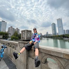 a man sitting on the edge of a bridge next to a bike and looking at the camera