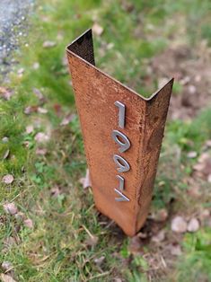 a rusted metal pole with the word love written on it sitting in grass next to a road