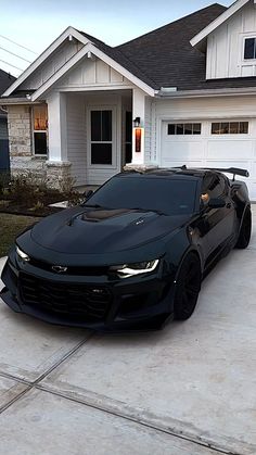 a black chevrolet camaro parked in front of a house