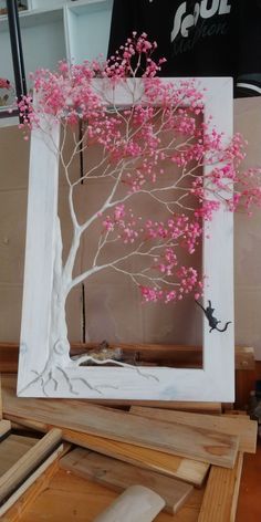 a white frame with pink flowers and a tree in the middle is sitting on top of plywood