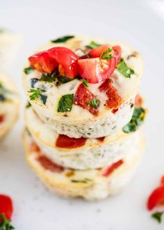 three mini pizzas stacked on top of each other with tomatoes and spinach in the middle