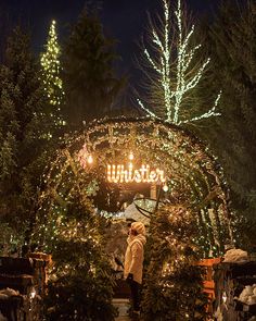 a woman standing in front of a lit up entrance to a christmas tree shop at night