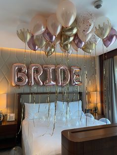 balloons are hanging from the ceiling in front of a bed with a bride sign above it