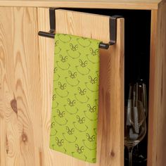 a kitchen cabinet with a green towel hanging from it's side door and wine glasses in the background