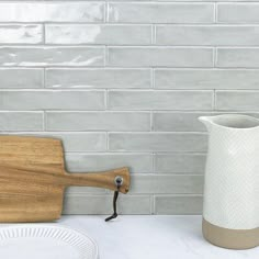 a white vase sitting on top of a counter next to a cutting board and plate