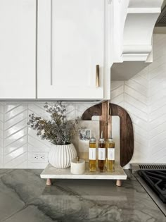 a kitchen with white cabinets and marble countertops is pictured in this image, there are two bottles of alcohol on the tray