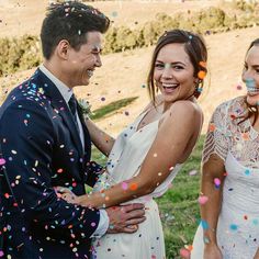 two brides and one groom are surrounded by confetti as they smile at each other