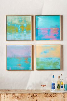 four abstract paintings hang on the wall above a buffet table with drinks and liquor bottles