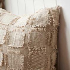 a close up of a pillow with fringes on the bottom and sides, against a white wall