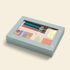 a blue box filled with assorted colored pencils and writing paper on top of a white surface