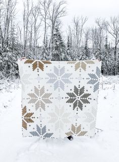 a white quilt with brown and gray snowflakes on it in front of some trees