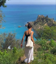 a woman with a bag walking up a hill near the ocean