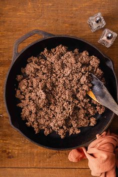 a skillet filled with ground beef on top of a wooden table next to ice cubes