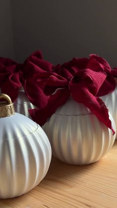 three white vases with red flowers in them sitting on a wooden counter top next to each other