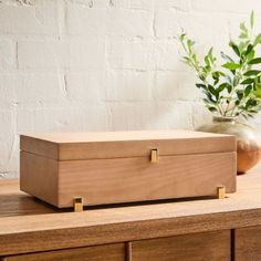 a wooden box sitting on top of a table next to a vase with green plants