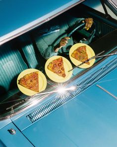 three slices of pizza on yellow plates in the back of a blue car, with a man sitting behind it