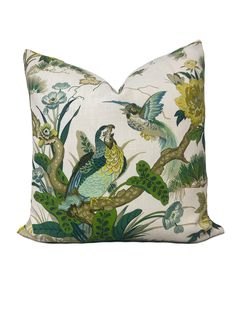 a white pillow with green and blue birds on the front, surrounded by leaves and flowers