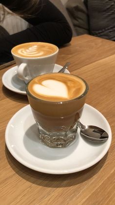 two cups of cappuccino sitting on top of a white plate next to each other