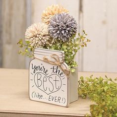 a vase filled with flowers sitting on top of a wooden table next to green plants