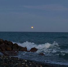 the moon is setting over the ocean and rocks