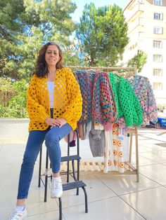 a woman sitting on a chair in front of some crocheted sweaters