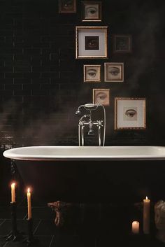 a white bath tub sitting next to candles and framed pictures on the wall above it