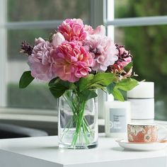 pink flowers in a glass vase on a table next to a cup and saucer