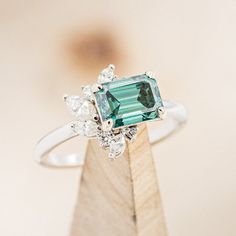 an emerald and diamond ring sitting on top of a wooden stand