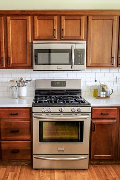 a stainless steel stove and microwave in a kitchen with wooden cabinets, white counter tops and wood flooring