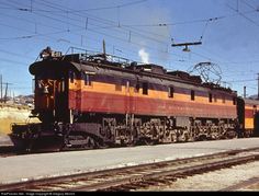 an orange and black train engine pulling its cars down the tracks with power lines above it