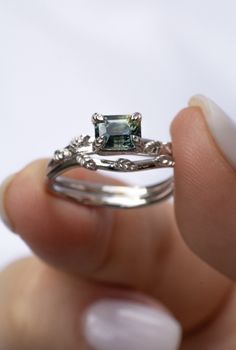 a woman's hand holding a ring with an emerald stone in it