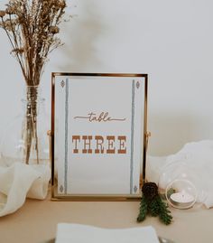 a table topped with a sign next to a glass vase filled with flowers and candles