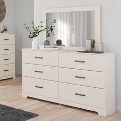 a white dresser and mirror in a room with hardwood floors, rugs and plants