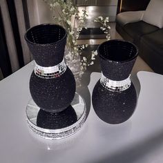 two black vases sitting on top of a white table next to a flower pot