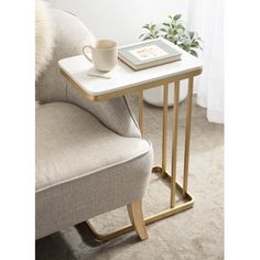 a white table with a book and cup on it next to a gray chair in front of a window