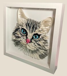 a white cat with blue eyes is in a shadow box on the wall and it appears to be made out of paper