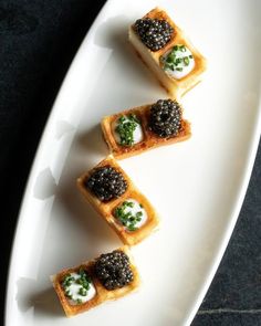 four pieces of food on a white plate with black cauliflower and green garnish