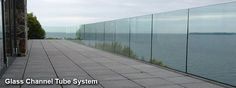 an empty walkway next to the ocean with glass walls on each side and water in the background