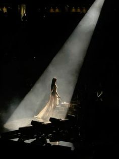 a woman in a white dress standing on stage with light streaming through her head and hands behind her back