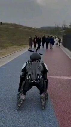 a man riding a motorcycle down a road with people walking on the side walk behind him