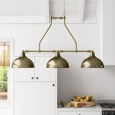 three lights hanging over a kitchen island in a white and gold colored room with wood flooring