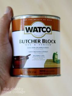 a hand holding a can of butcher block paint in it's left hand,