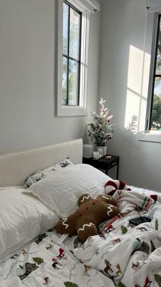 a teddy bear laying on top of a bed in a bedroom next to two windows